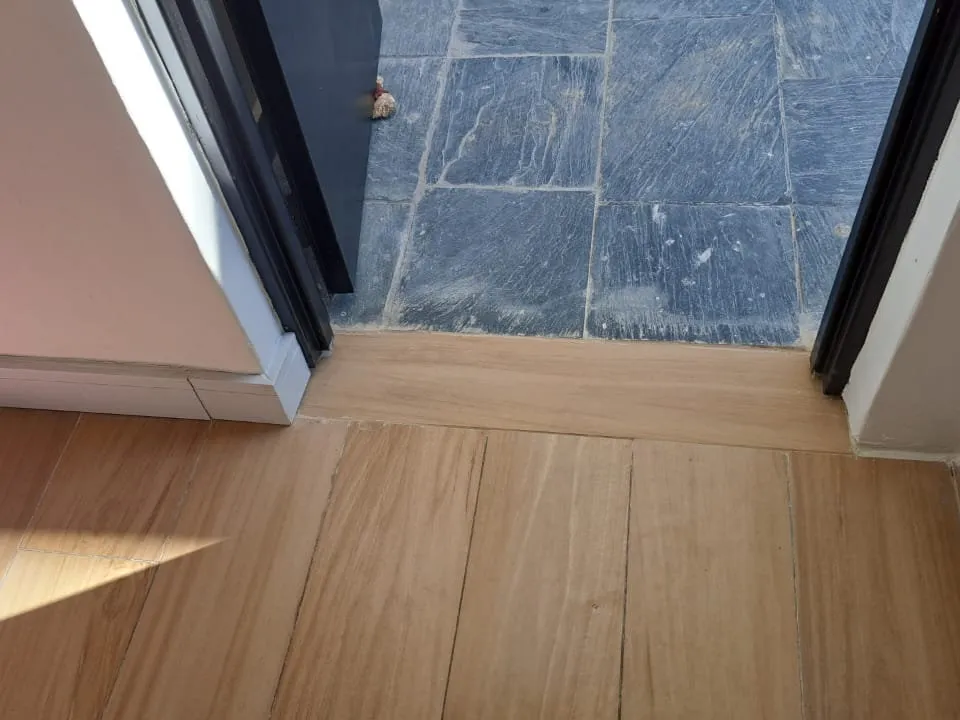 Umbral símil madera entre el piso interior y las baldosas grises del patio, con marcos de puerta a los lados.